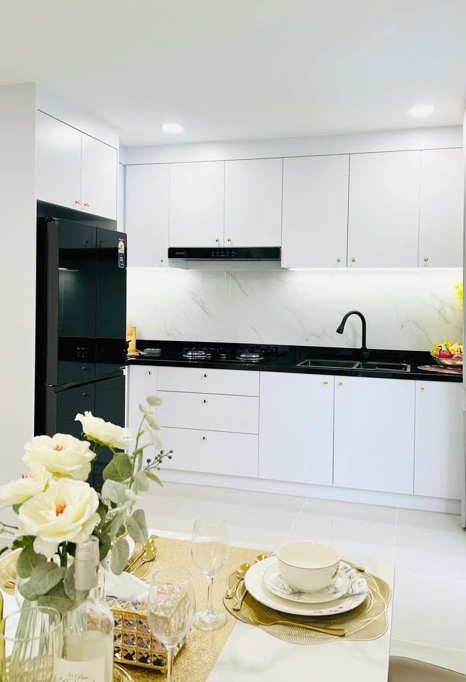 Modern kitchen with white cabinets, black countertops, marble backsplash, and a dining table set with flowers and gold accents in the foreground