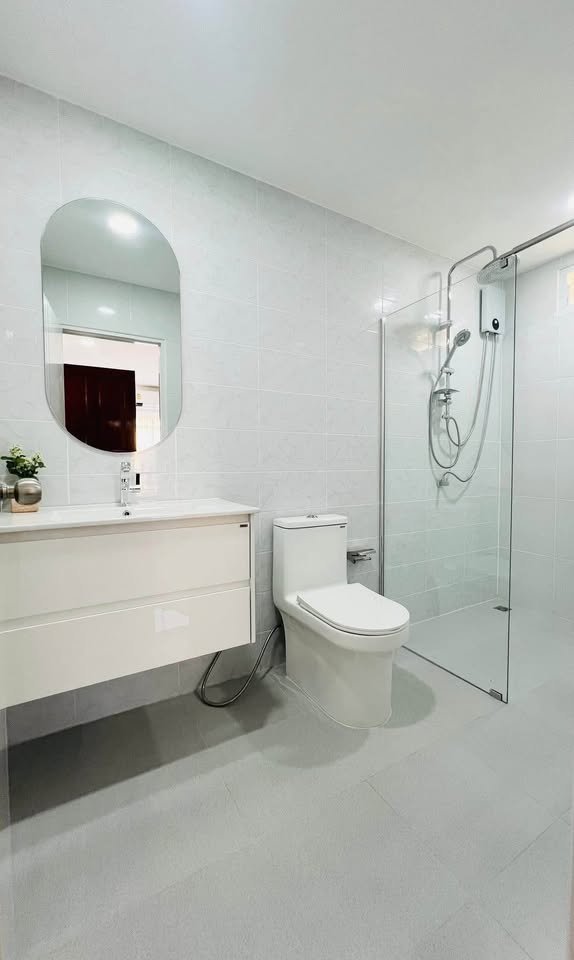 Modern white bathroom with floating vanity, oval mirror, toilet, and glass-enclosed shower stall