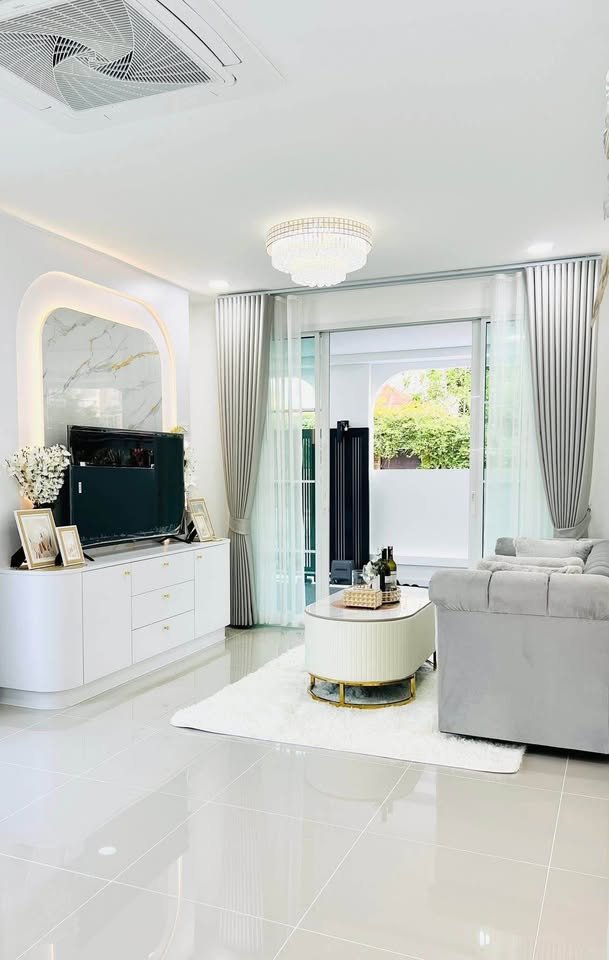 Bright modern living room with white and gold decor, TV console, round coffee table, gray sofa, and sheer curtains