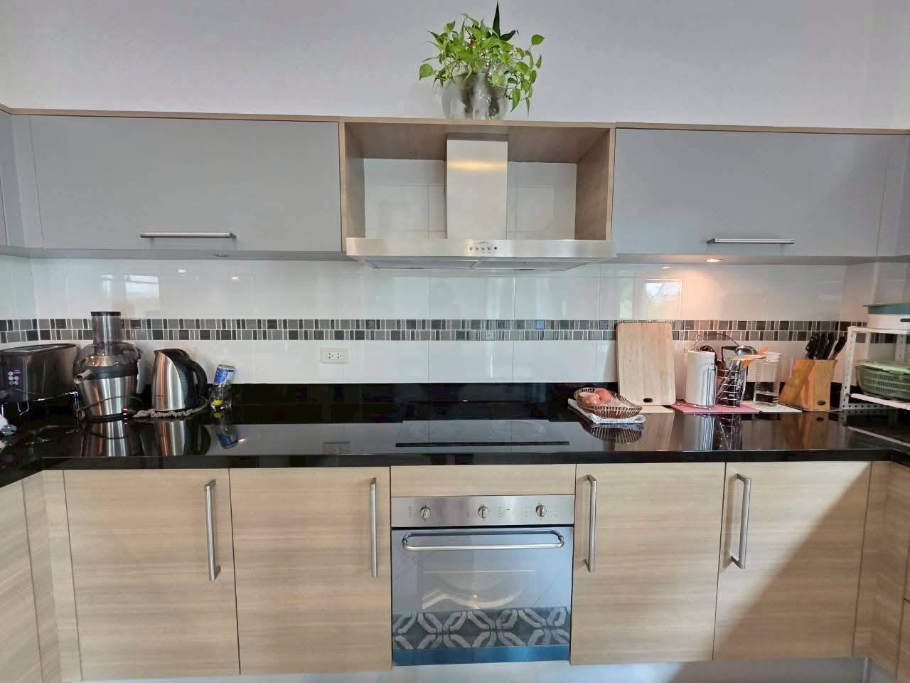 Kitchen with black granite countertops, built-in oven, range hood, light wood cabinets, and small appliances including a kettle and juicer