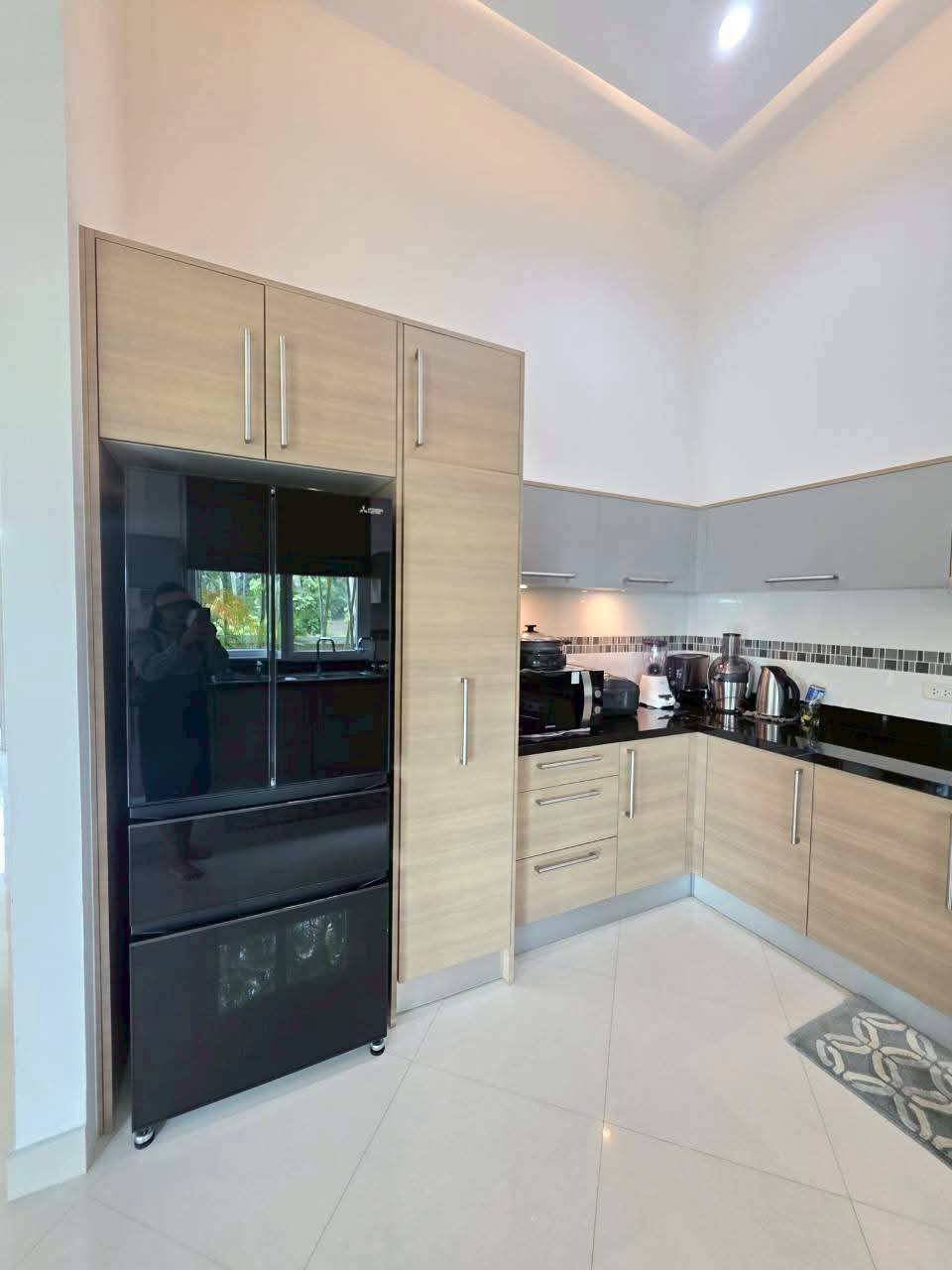 Modern kitchen with light wood cabinetry, black French-door refrigerator, dark granite countertops, and small appliances along the backsplash