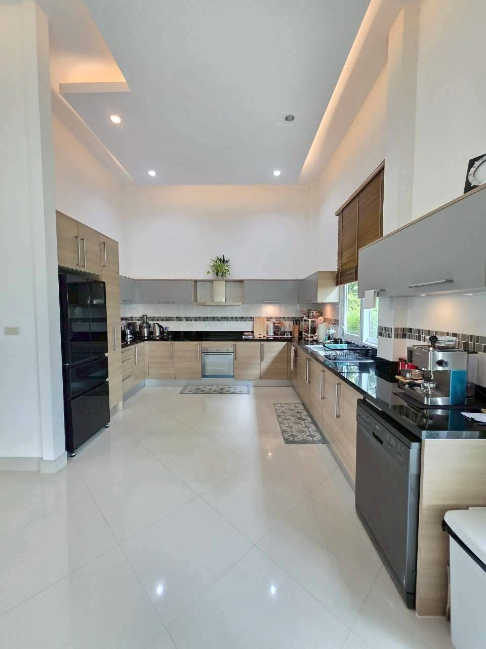 Spacious modern kitchen with wood-tone cabinetry, black countertops, built-in oven, refrigerator, and tiled flooring