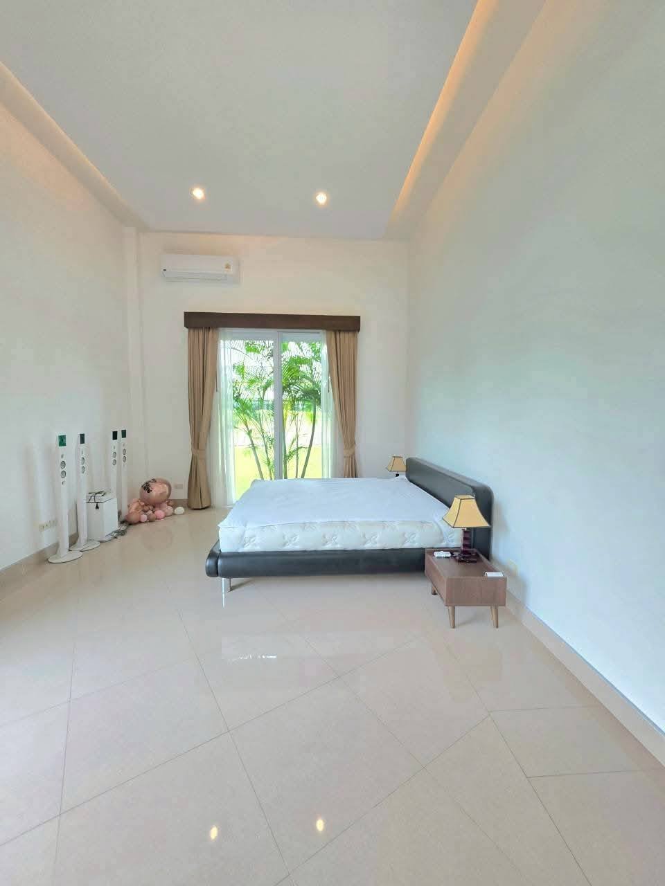 Spacious bedroom with a low-profile bed, tray ceiling with recessed lighting, air conditioning unit, and sliding glass door with garden view
