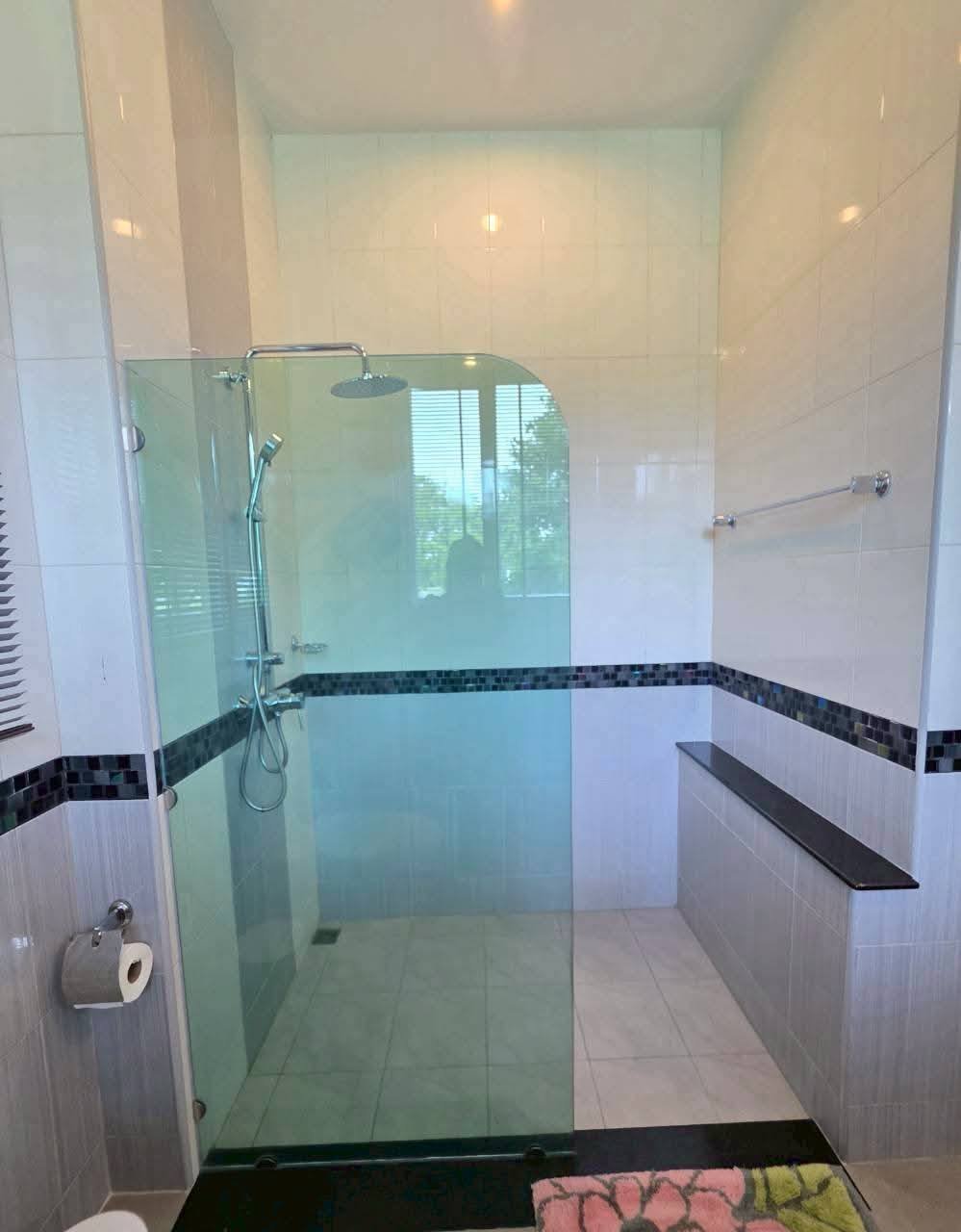 Spacious walk-in shower with glass panel, rain showerhead, built-in bench, and mosaic tile accent border