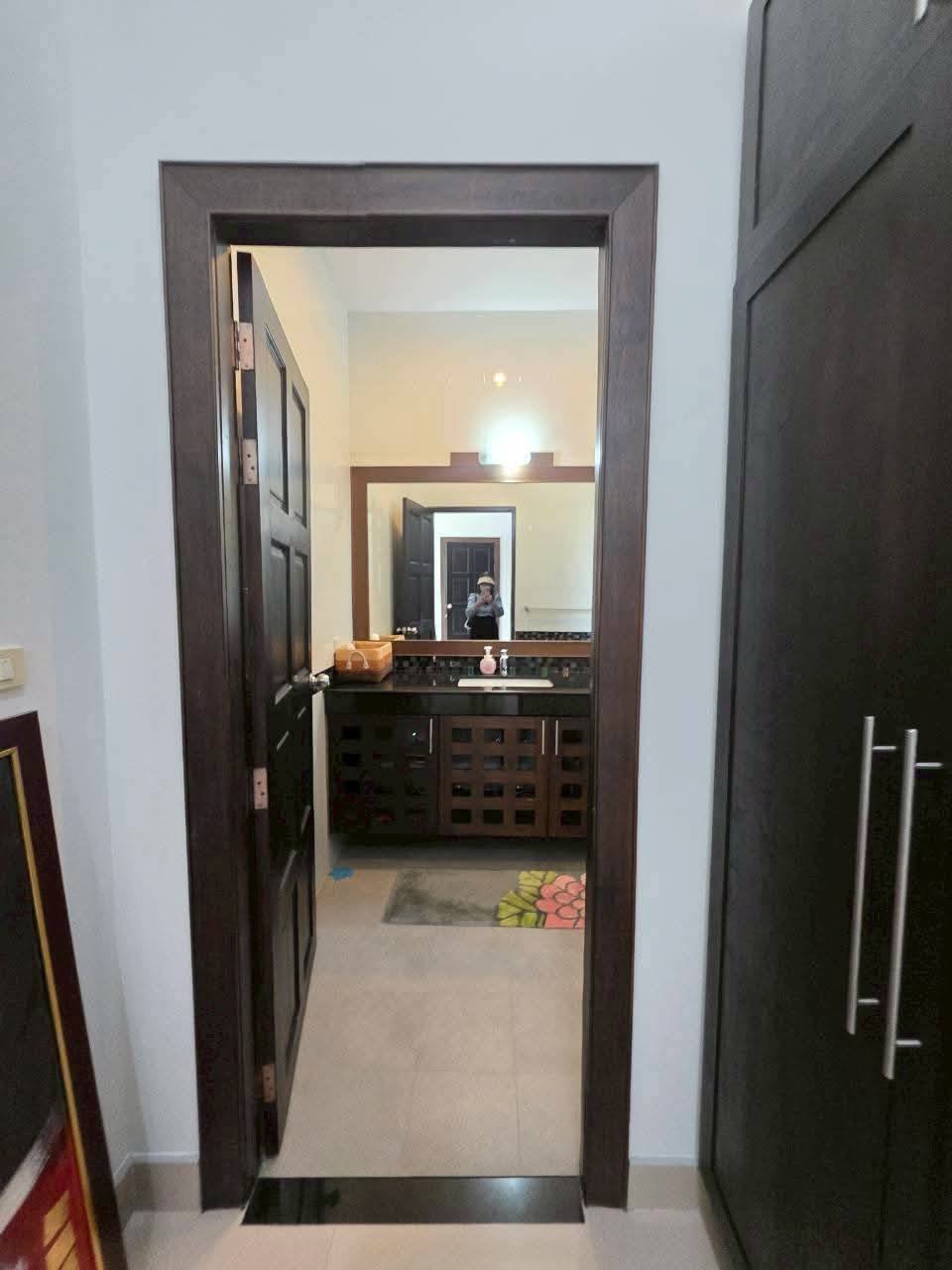 Bathroom entrance with dark wood door frame, vanity with dark cabinetry, and a large mirror reflecting the photographer