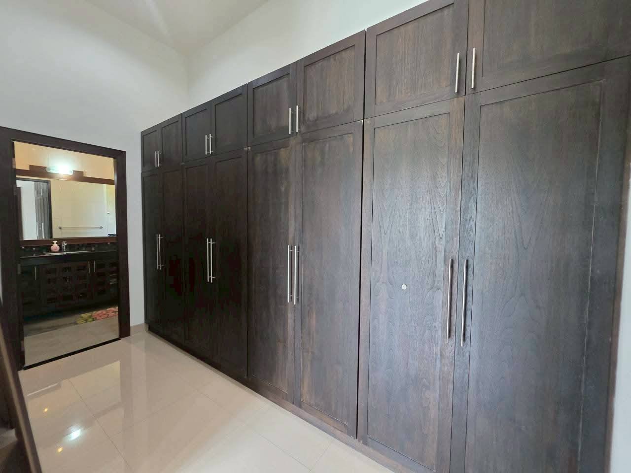Bedroom with floor-to-ceiling dark wood built-in wardrobes with silver bar handles, and an en-suite bathroom visible through a doorway