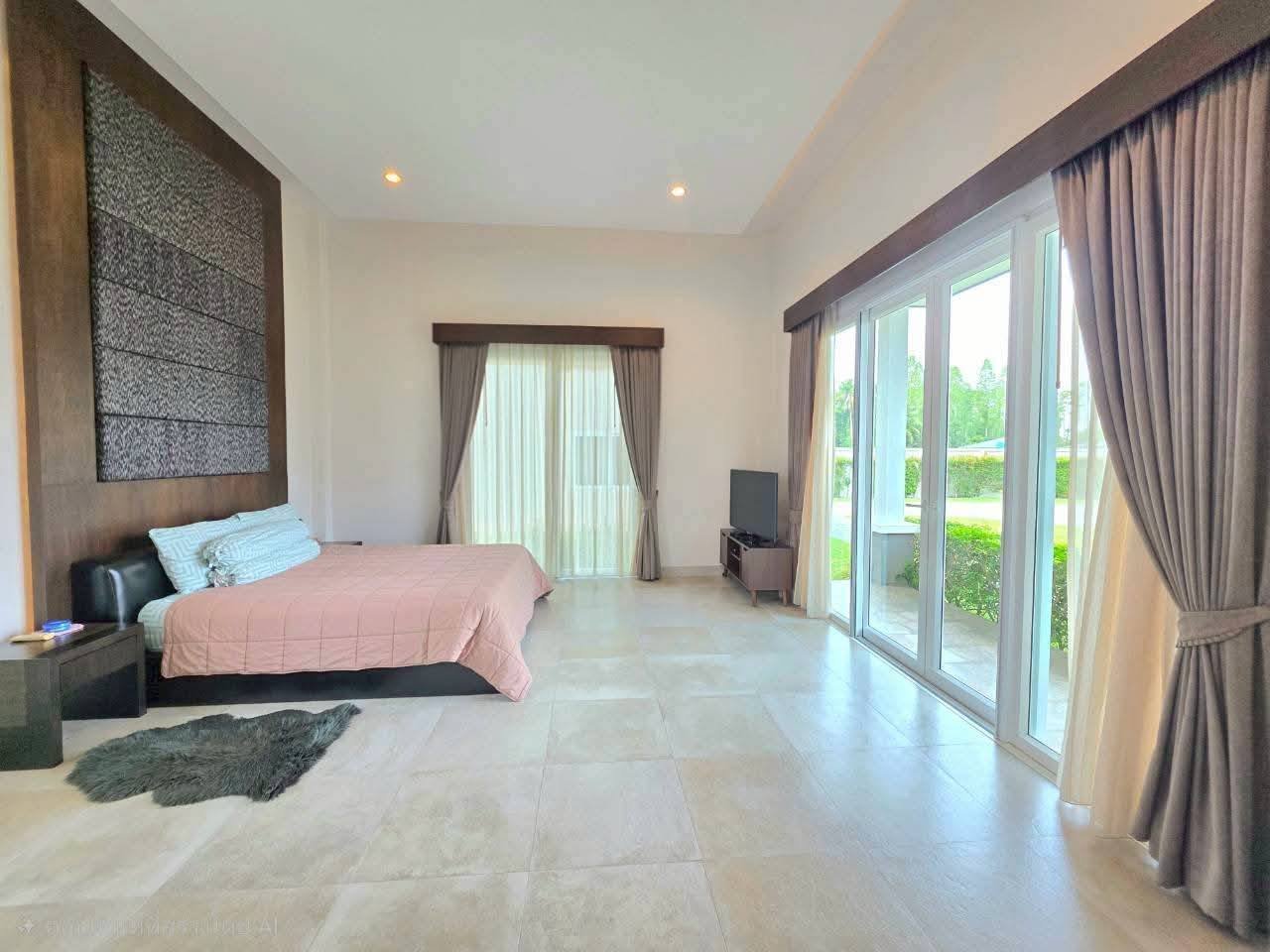 Spacious bedroom with a queen bed, textured wood accent wall, TV, and sliding glass doors opening to a garden view