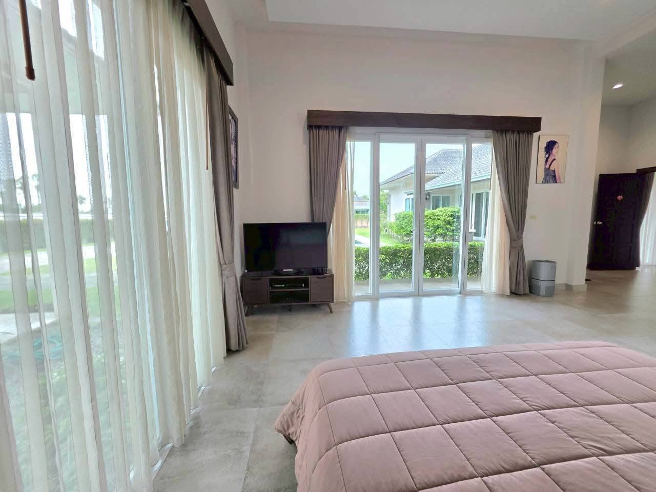 Spacious bedroom with a pink bedspread, flat-screen TV, sheer curtains, and glass doors opening to a garden view