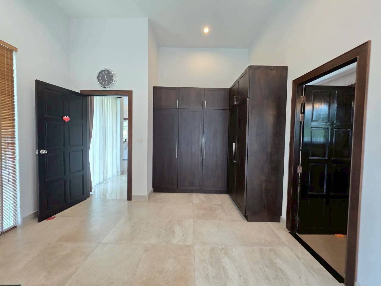 Spacious bedroom with dark wood built-in wardrobes, marble tile flooring, high ceilings, and two dark wood doors