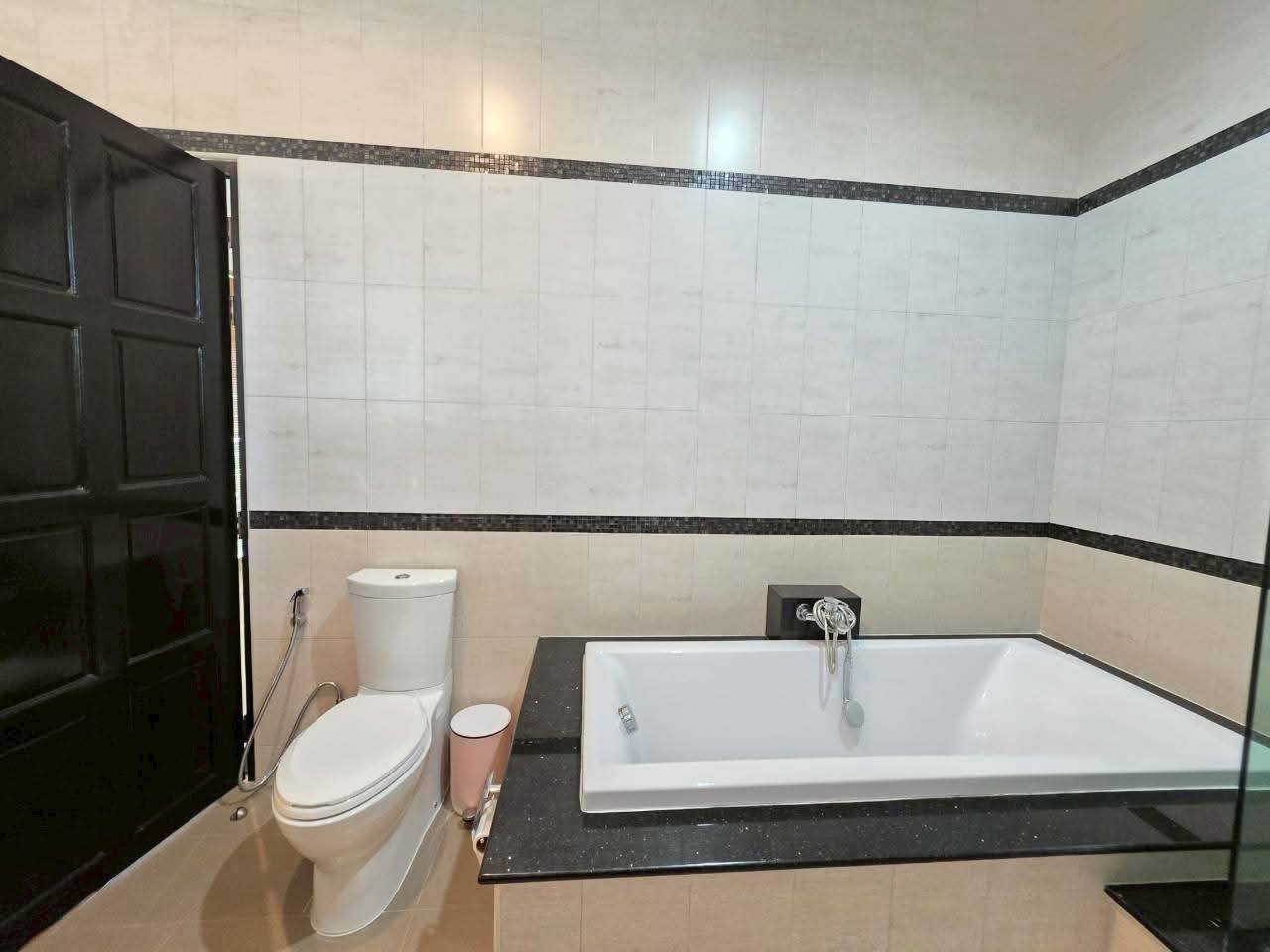 Bathroom with a white soaking tub set in a dark granite surround, toilet, and white tile walls with mosaic border accents