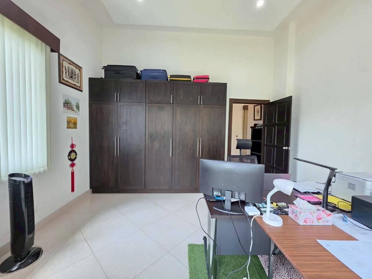 Home office with a dark wood wardrobe, desk with monitor, and luggage stored on top of the cabinet