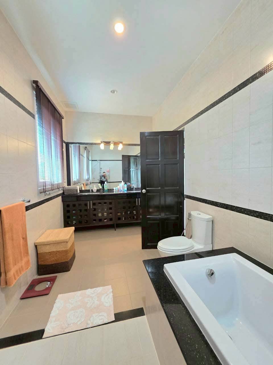 Spacious bathroom with a soaking tub, toilet, dark wood vanity with mirror, tiled walls, and a window with blinds