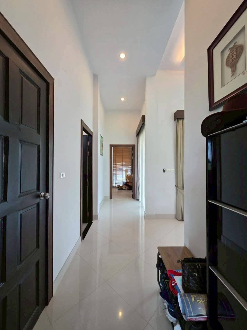 Bright hallway with white tile floors, dark wood doors, recessed lighting, and a bedroom with natural light at the end