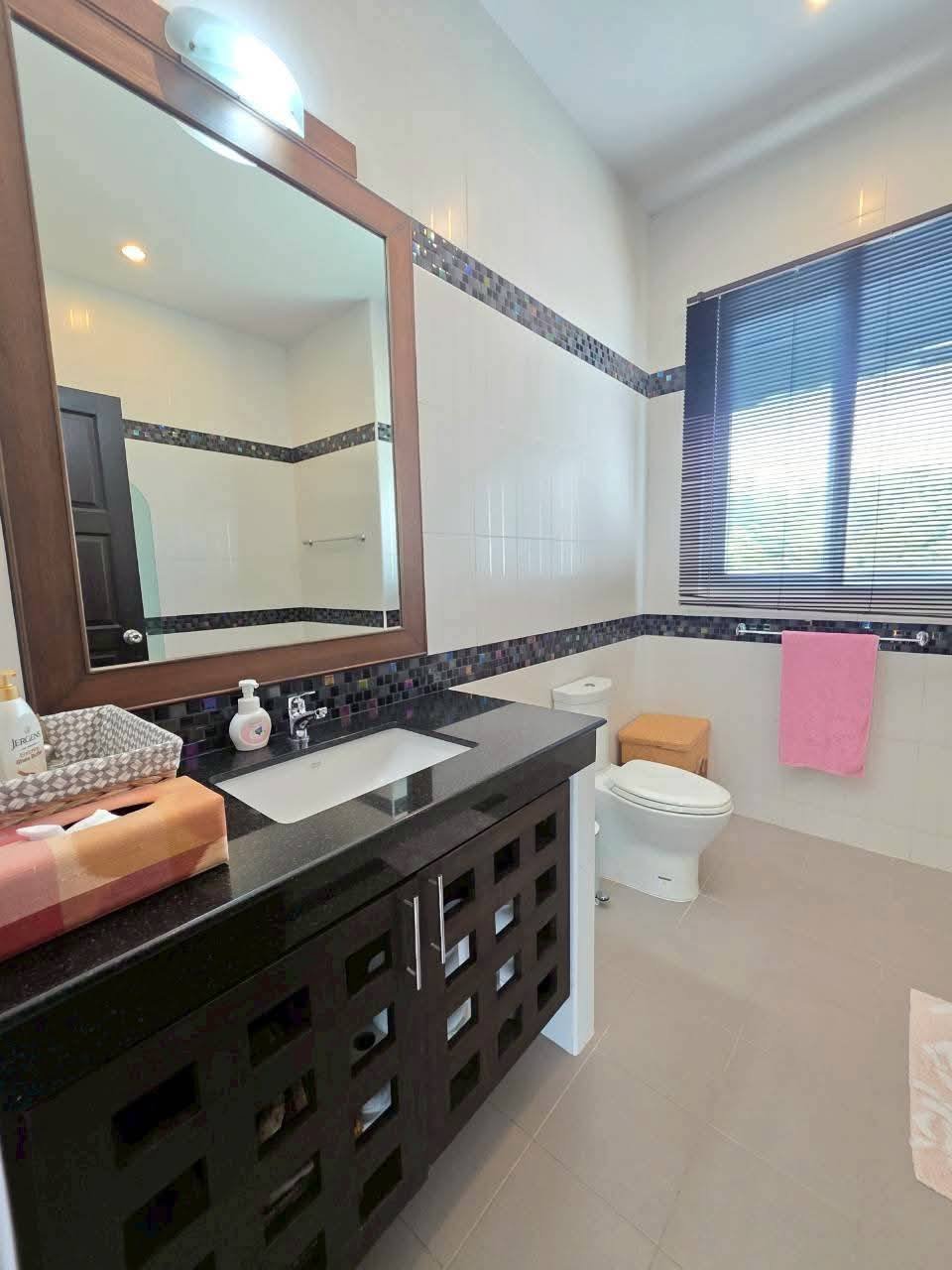 Bathroom with dark wood vanity, black granite countertop, framed mirror, mosaic tile accent border, toilet, and window with blinds