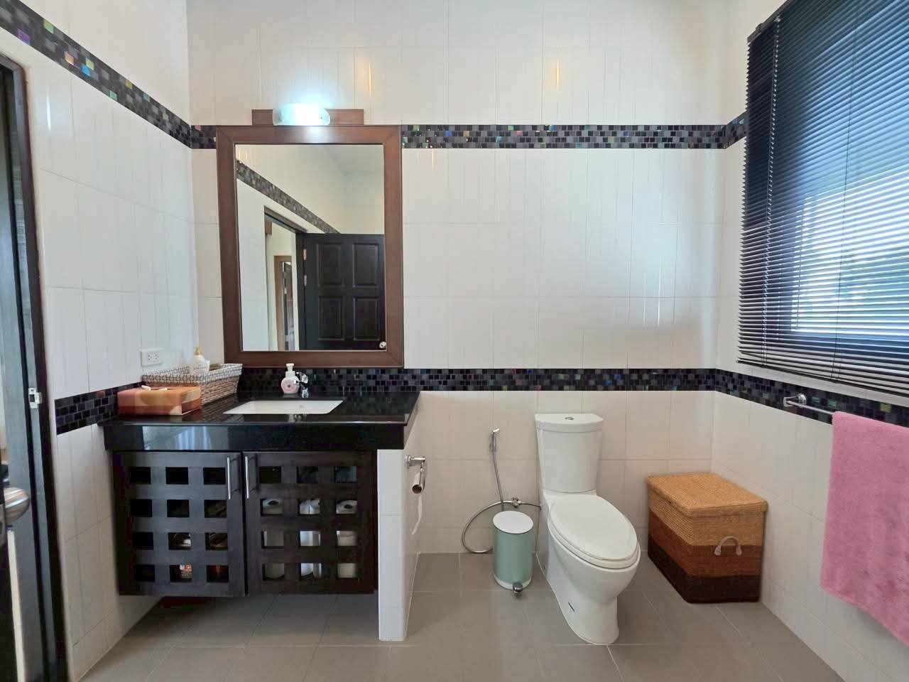 Bathroom with dark vanity, black granite countertop, mosaic tile accent border, framed mirror, and toilet with window blinds