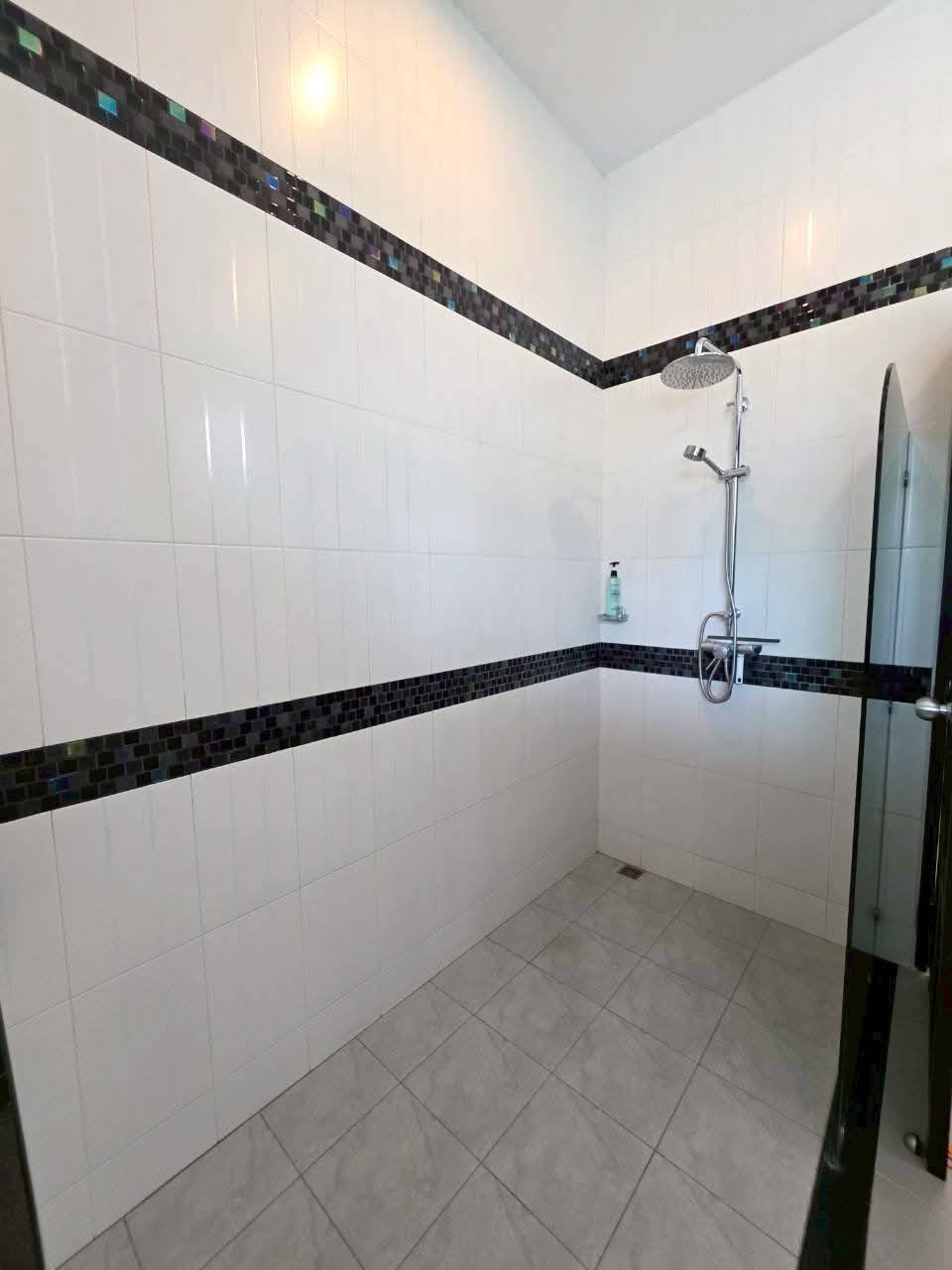 Walk-in shower with white tiles, iridescent mosaic border strips, and a chrome rain showerhead with sliding bar