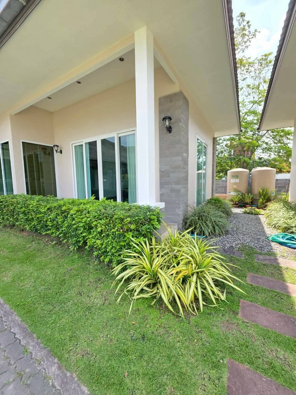 Exterior of a single-story house with large sliding glass doors, stone accent column, wall lanterns, and a well-maintained lawn with tropical plants