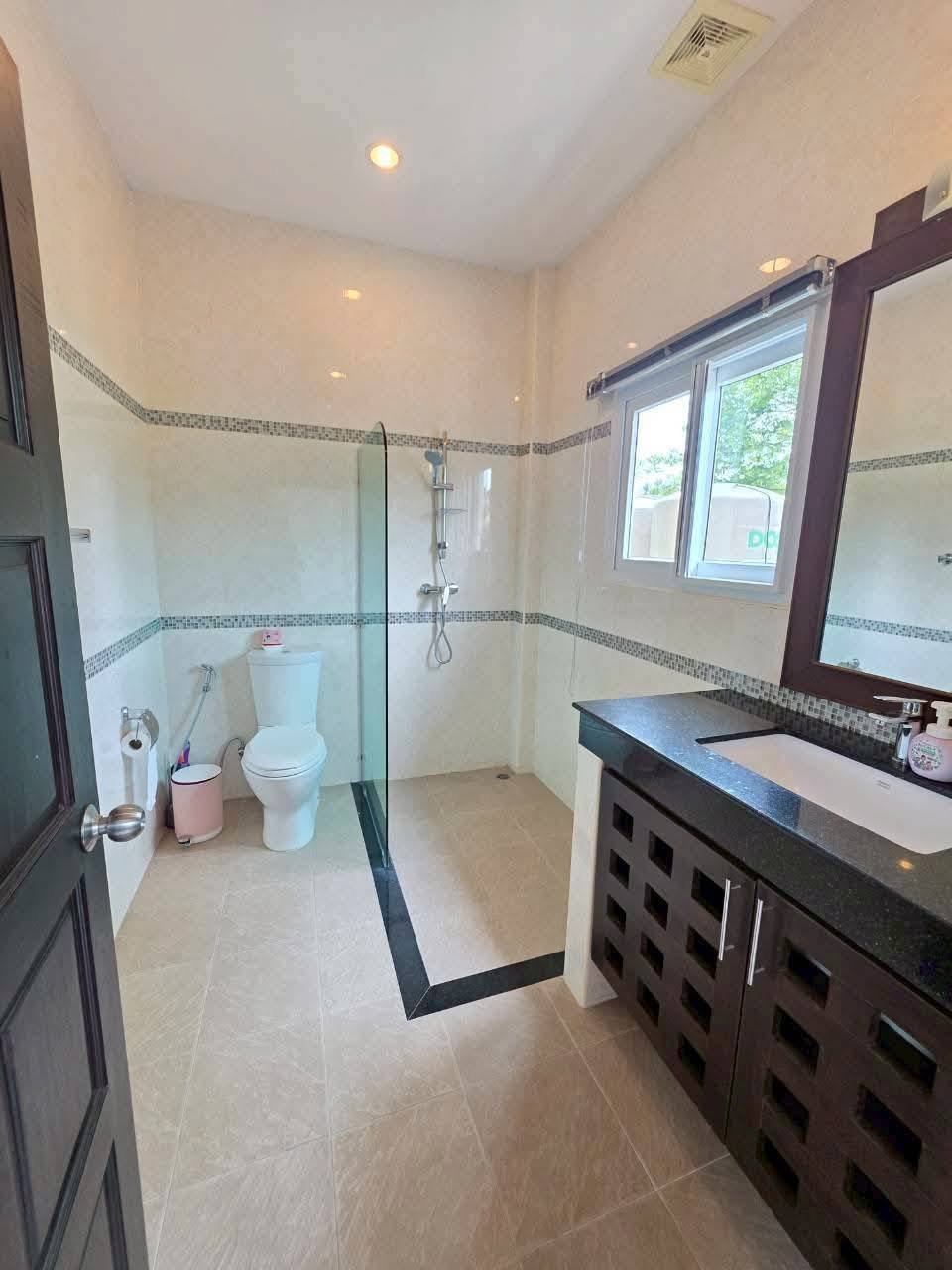 Bathroom with glass-enclosed shower, toilet, dark wood vanity with black granite countertop, and mosaic tile accent border