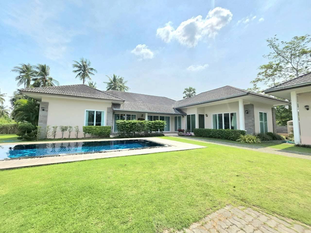 Single-story villa exterior with a private swimming pool, manicured lawn, and tropical palm trees in the background