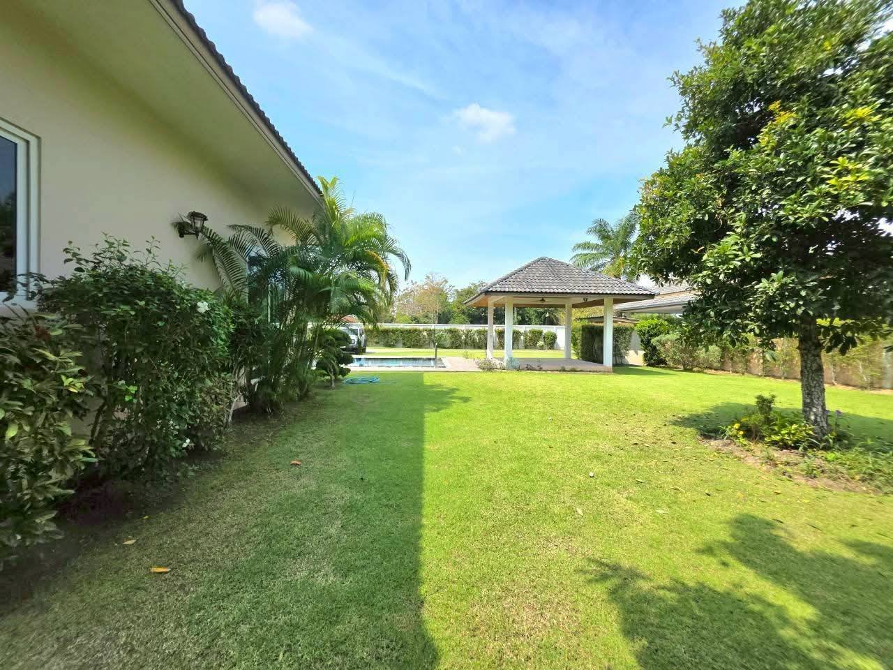 Spacious backyard with manicured lawn, gazebo, swimming pool, and tropical trees alongside a single-story house