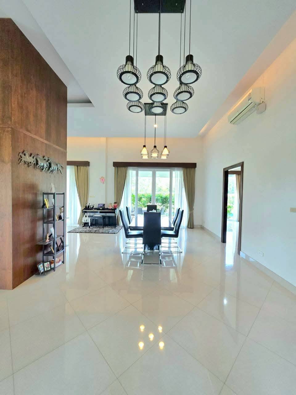 Spacious open-plan dining area with high ceilings, cluster pendant lights, black dining set, polished tile floors, and large windows