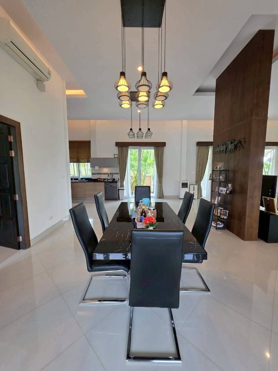 Open-plan dining area with a black marble table, six black leather chairs, and a cluster pendant light, with kitchen visible in background