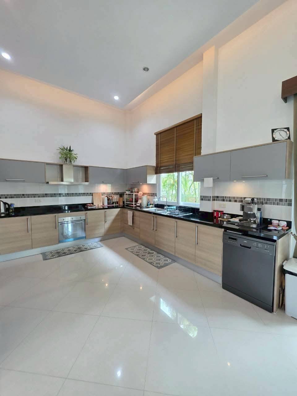Spacious modern kitchen with wood and gray cabinetry, black countertops, oven, dishwasher, and high ceilings with recessed lighting