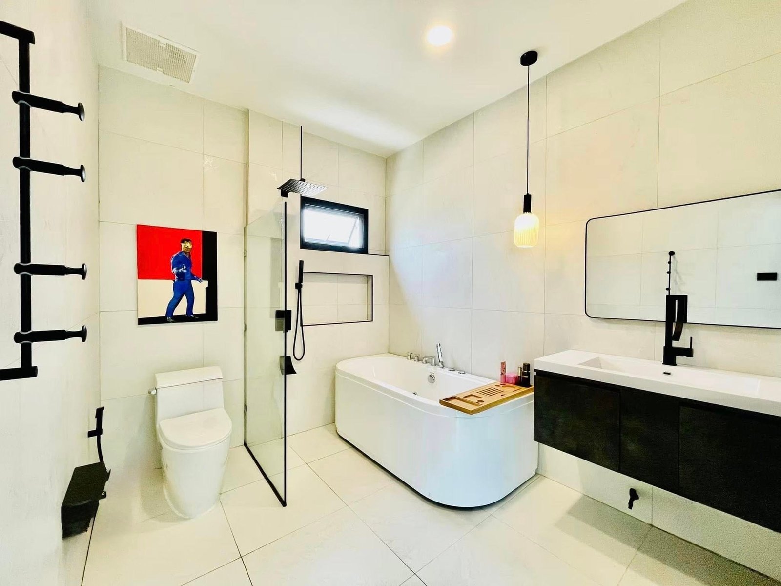 Modern bathroom with freestanding soaking tub, walk-in shower, floating dark vanity, black fixtures, and a colorful artwork on the wall