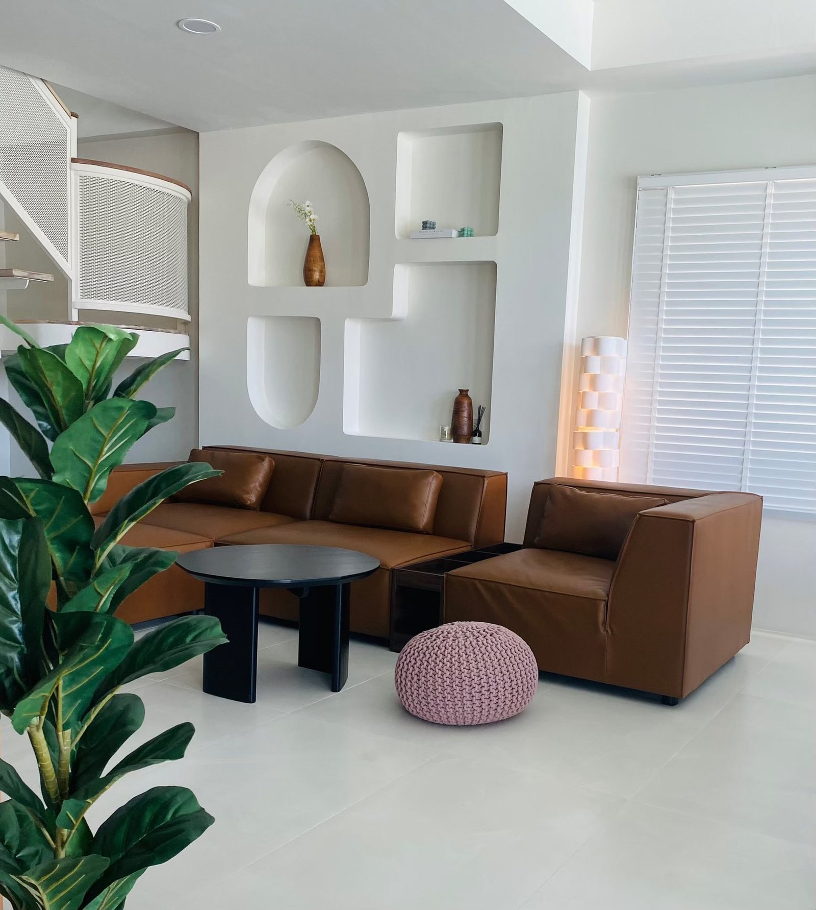 Modern living room with tan leather sofa and chair, black round coffee table, pink knit pouf, and sculptural built-in wall niches