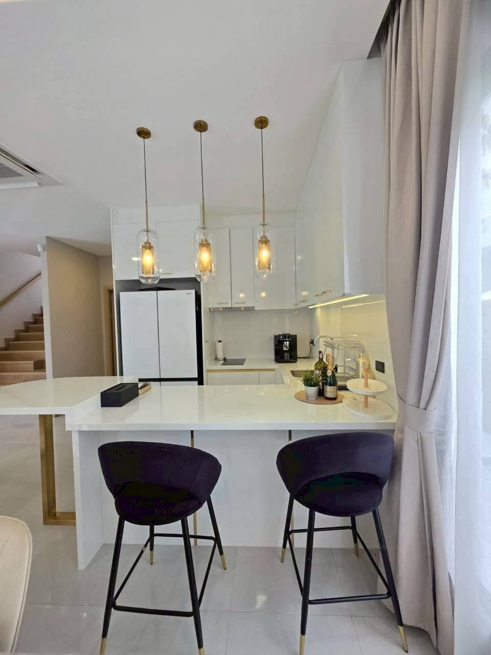 Modern kitchen with white cabinetry, pendant lights, and black bar stools