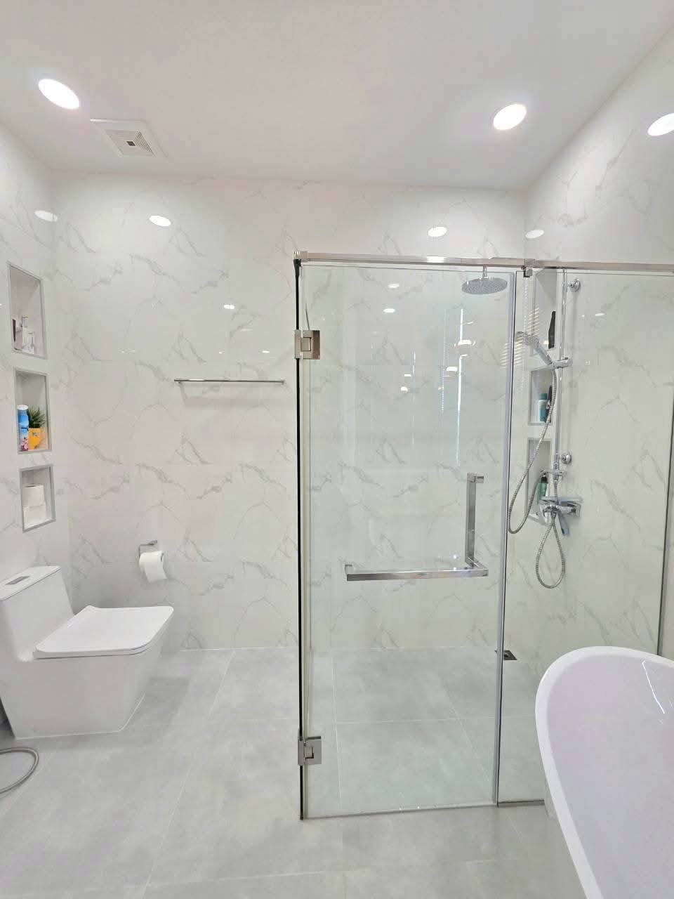 Modern luxury bathroom with marble walls, glass shower enclosure, freestanding tub