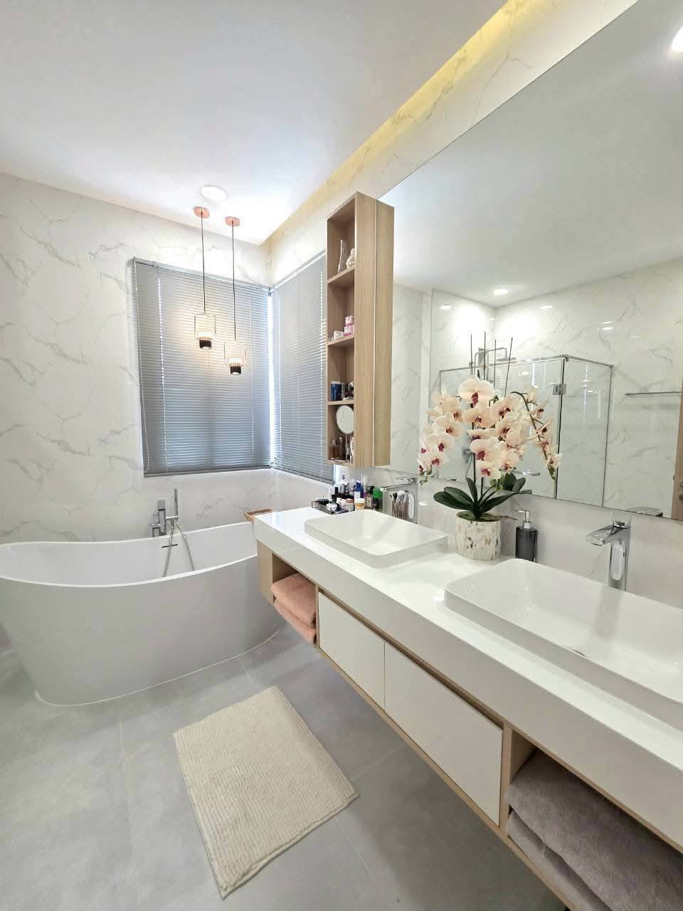 Modern luxury bathroom with marble walls, dual sinks, soaking tub, and orchid flowers