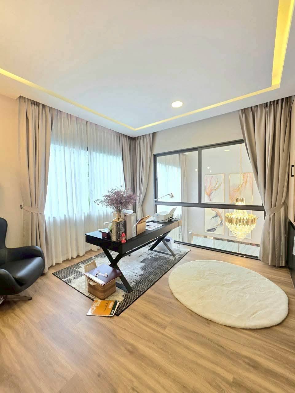 Modern office space with desk, neutral curtains, wooden flooring, and ceiling lighting