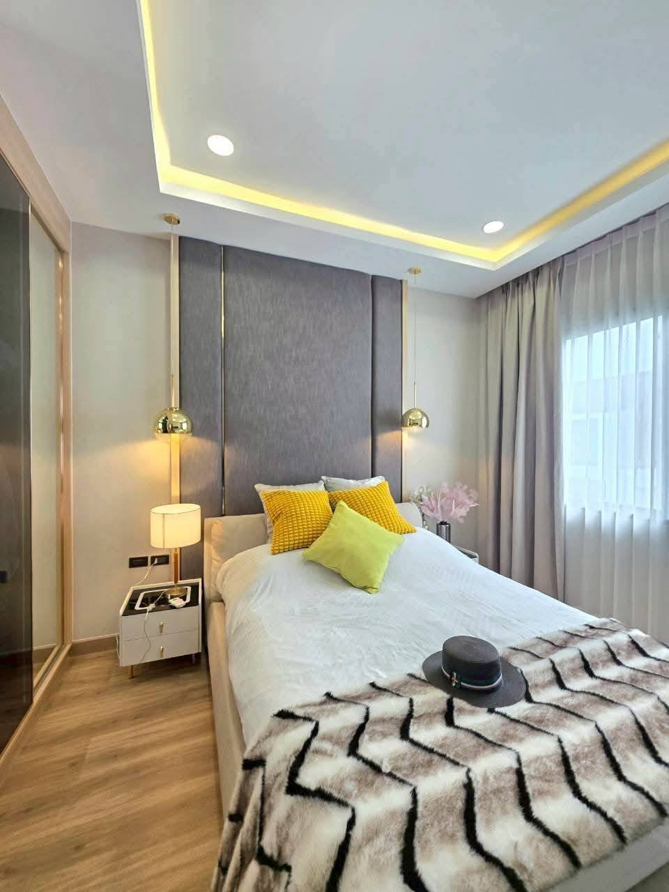 Modern bedroom with gray headboard, yellow pillows, pendant lights, and geometric patterned bedding