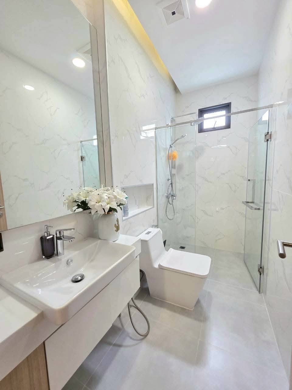 Modern white bathroom with marble tiles, glass shower enclosure, and vessel sink
