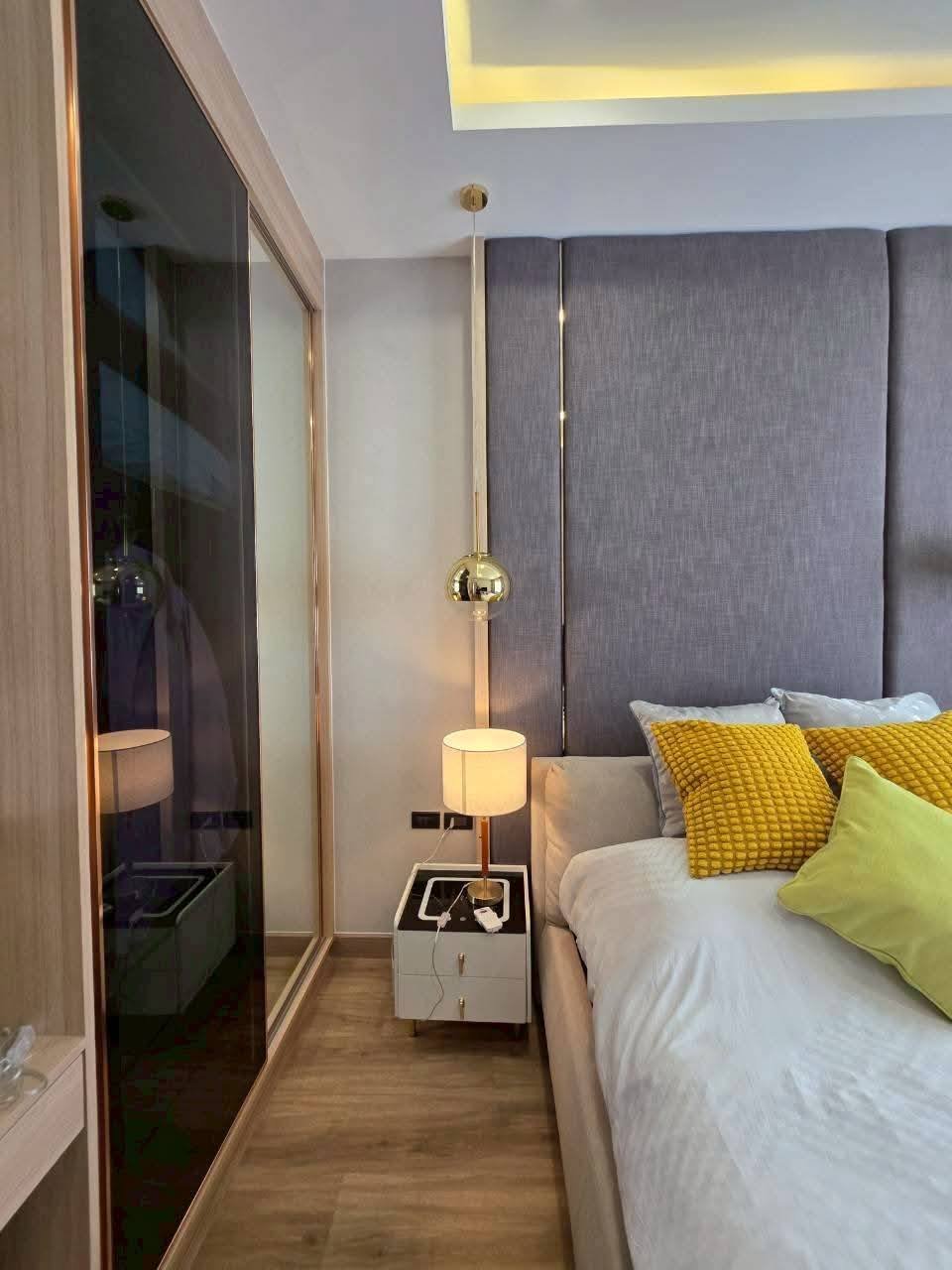 Modern bedroom with gray headboard, yellow pillows, brass pendant lamp, and mirrored closet door
