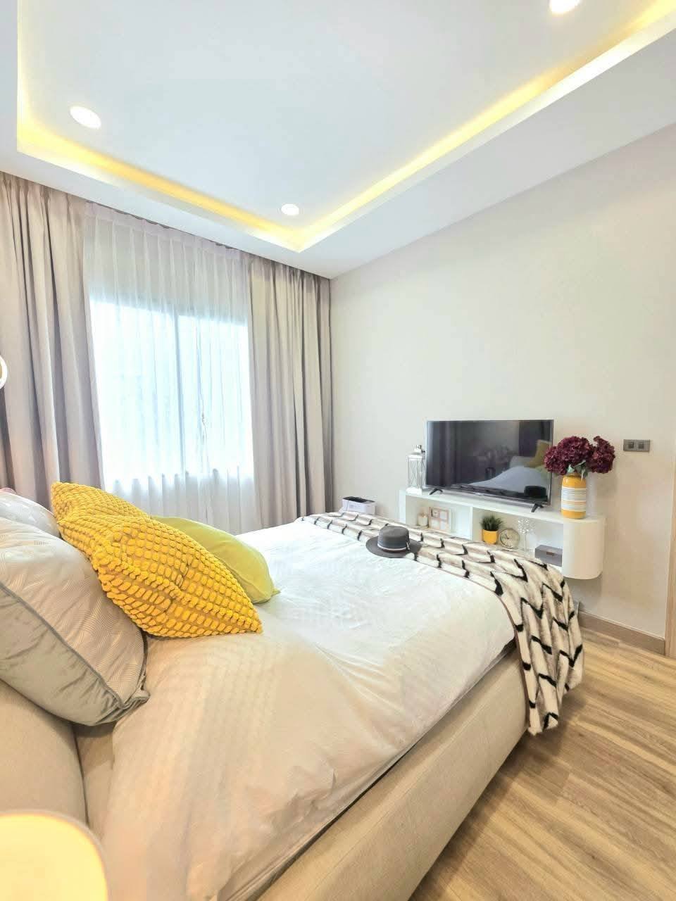 Modern bedroom with yellow accent pillows, TV stand, and recessed ceiling lighting