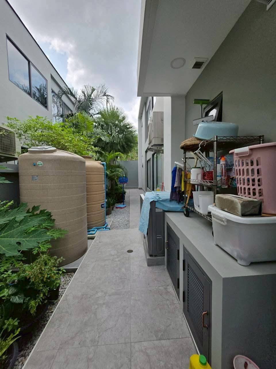 Narrow side yard with water storage tanks, laundry items, and tropical plants